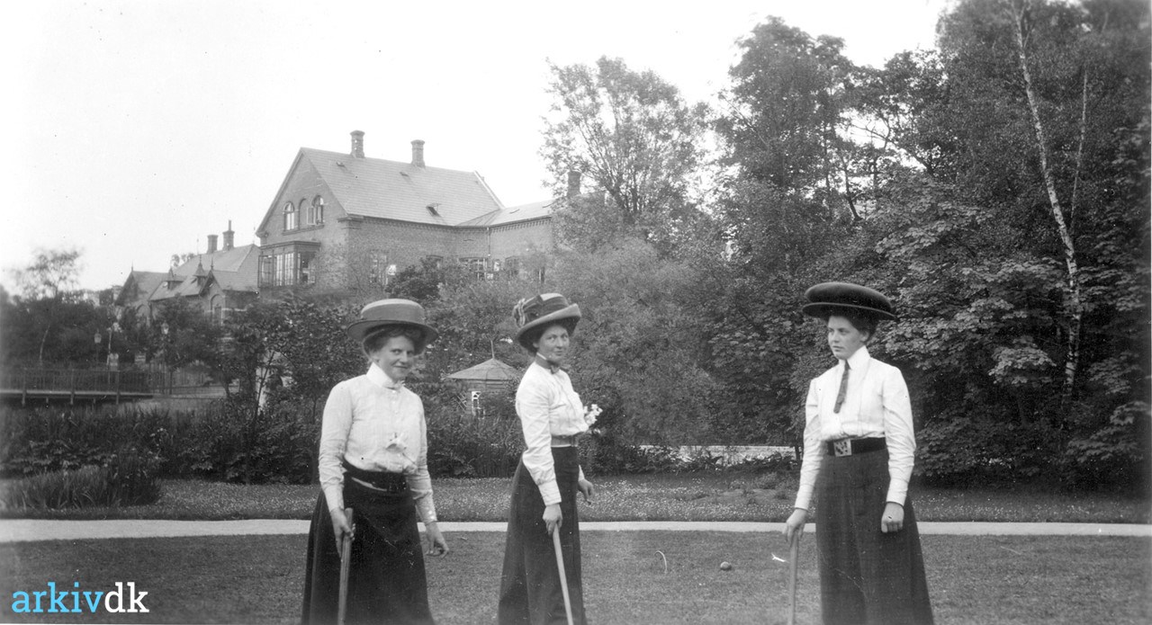 | Damer spiller kroket, ca. 1913. Tre damer med hatte og lange kjoler spiller i Læseforeningens Have i Odense.